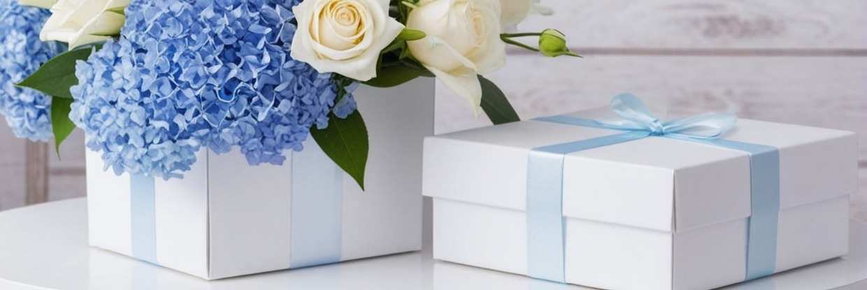 Поздравительный букет с белыми розами и синими гортензиями, украшенный подарочными коробками с голубыми лентами на светлом фоне. Элегантная праздничная композиция.
